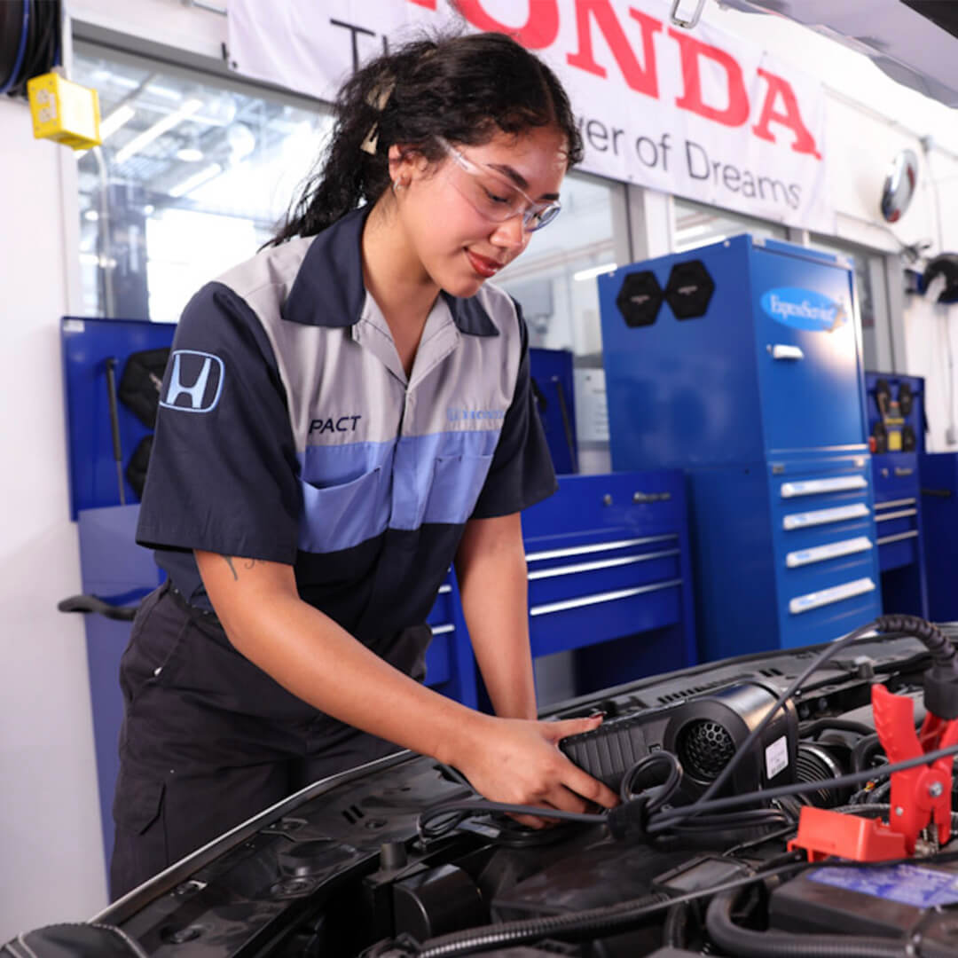 Female HondaPACT student working under hood of vehicle.